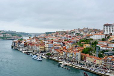 Porto, güzel nehir kıyısını Douro Nehri boyunca renkli binalarıyla sergiliyor. Turistler eşsiz mimari ve dingin su manzaralarının tadını çıkararak rıhtımda geziniyorlar..