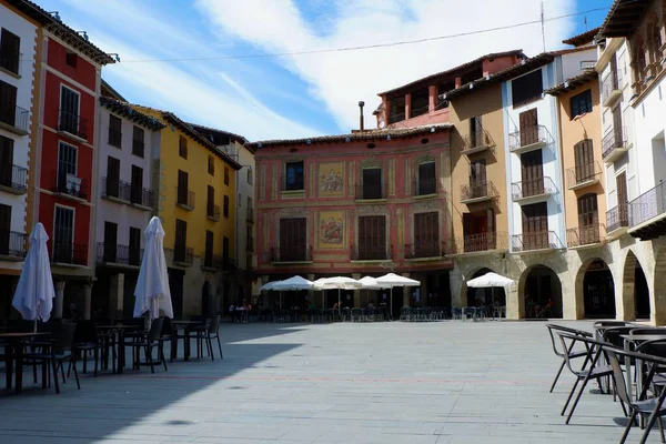 Meydanda balkonlu renkli binalar, boş masalar, sandalyeler ve güzel duvar resimleri yer alıyor. Parlak gökyüzü rahatlamak için mükemmel bir atmosfer yaratır..