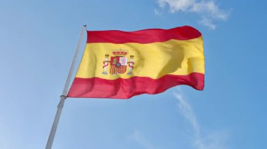 İspanya bayrağı açık havada hafif rüzgarla mavi gökyüzüne doğru sallanıyor.