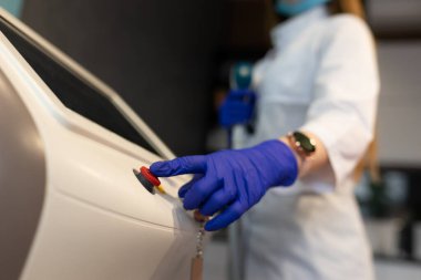 Kadın lazer epilasyon makinesindeki kırmızı düğmeye basıyor.