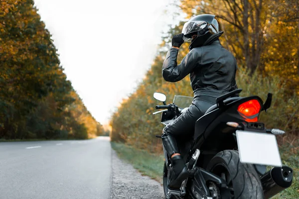 Yol kenarında deri kıyafetli bir motosikletli.