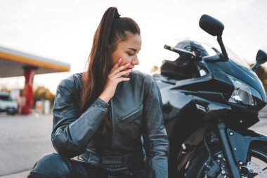 Motosikletinin yanında deri takım elbiseli bisikletçi kız.