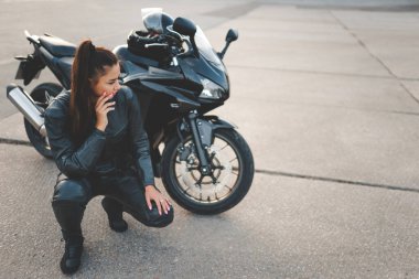 Motosikletinin yanında deri takım elbiseli bisikletçi kız.
