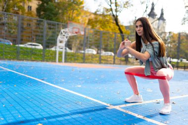 Atletik kadın direniş bantlarıyla çömeliyor.