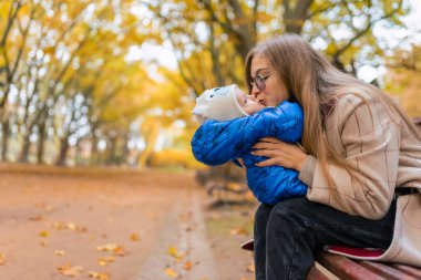 Parktaki bankta elinde bebek olan bir anne. Anne bebeği öpüyor.