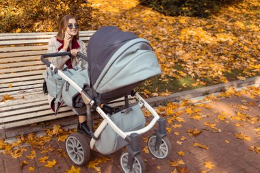 Bebek arabalı şık anne, çocuk uyurken parkta bankta otururken telefonla konuşuyor.