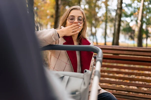 Sleepy mom yawns while sitting on park bench