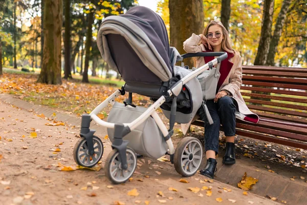 Mother with stroller while walking in the park sat down on bench to rest