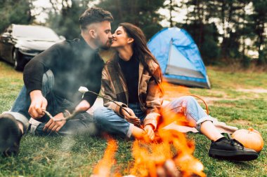 Kavrulmuş lokum elleriyle kamp ateşinin yanında oturan romantik çift öpüşüyor.