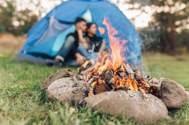 Çadırda yalnız oturan aşıklar kamp ateşinin yanında, seçici bir odak noktası.