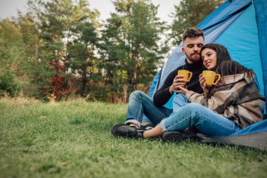 Romantik bir çift ellerinde çay fincanlarıyla çadırın yanında oturuyor.