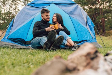 Çadırın yanında oturmuş çay içen neşeli turistler.