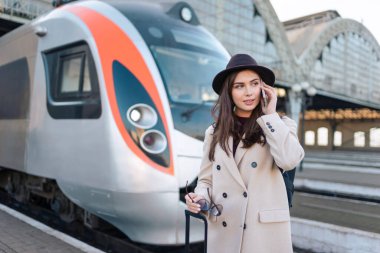 Trenin arka planında, platformda beklerken telefonda konuşan güzel bir bayan turist.