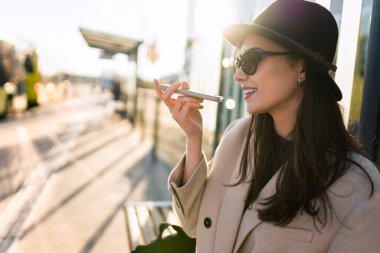 Otobüs durağında otururken hoparlörde konuşan kız.