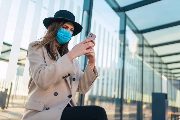 Meisje Met Beschermend Masker Zit Bij Bushalte Met Telefoon Handen — Stockfoto