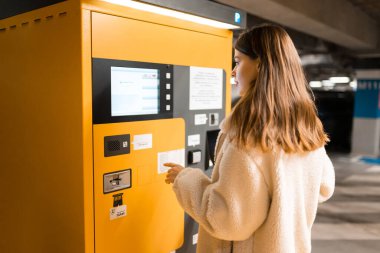 Zarif genç kız cezayı park metreyle ödüyor. Terminalin yanındaki otoparkta bir kadın var.