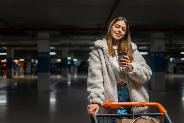 Schöne Mädchen Mit Tasse Kaffee Und Einkaufswagen Der Tiefgarage Des — Stockfoto