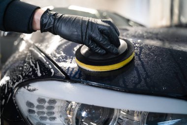 Adam arabanın kaputunu süngerle temizliyor. Otomatik parlatılmaya hazırlanıyor.