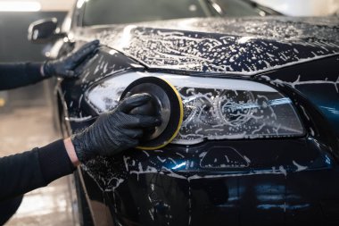 Adam araba lambasını daire şeklinde süngerle temizliyor. Otomatik parlatılmaya hazırlanıyor.