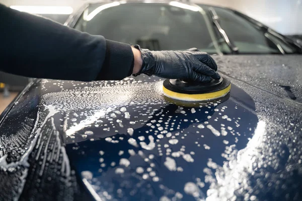 Man cleans car hood with circle sponge. Preparing auto for polishing.