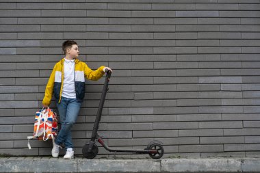 Sırt çantalı ve duvarda elektrikli scooter olan bir genç. Modern okul çocuğu konsepti