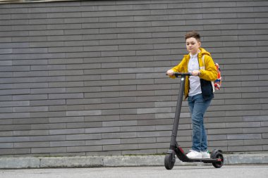 Sırt çantalı modern bir genç, arka planda elektrikli scooter kullanıyor. Çocuk okuldan dönüyor.