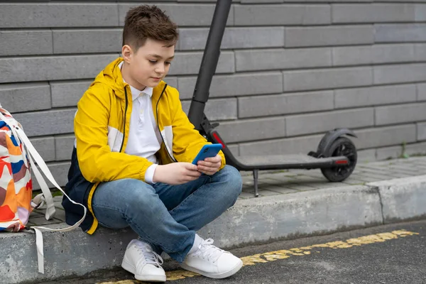 Nastolatek Telefonem Komórkowym Siedzący Obok Skutera Elektrycznego Plecaka Nowoczesny Młody — Zdjęcie stockowe