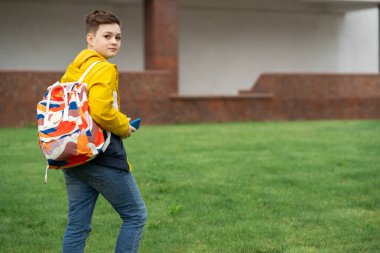 Sırt çantalı öğrenci yeşil çimlerde yürüyor.
