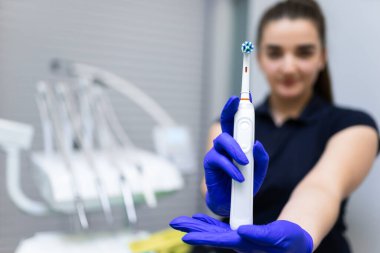 Kadın dişçi elinde elektrikli diş fırçası tutuyor.