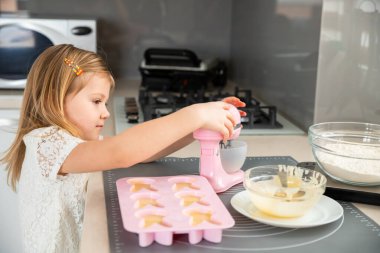 Küçük kız kek pişirmek için mikser kullanıyor.