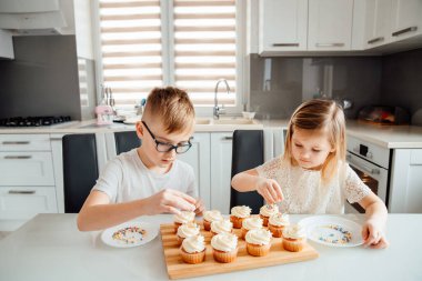 İki çocuk üzerine krema serpiştirerek kek süslüyor.