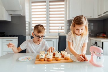 İki çocuk üzerine krema serpiştirerek kek süslüyor.