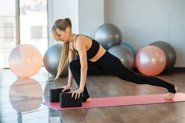 İnce kız yoga bloklarıyla esneme hareketleri yapıyor.