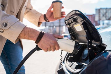 Şık bir adam şarj aletinin prizini yakın plan elektrikli arabanın prizine takar.