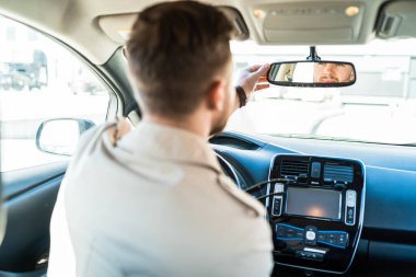 Sürücü dikiz aynasına bakar. Adam arabadaki aynayı ayarlıyor.