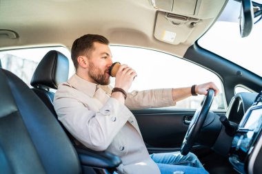 Adam araba kullanırken sabah kahvesi içiyor.