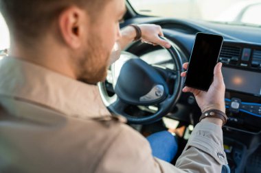 Elinde akıllı bir telefonla araba süren bir adam..