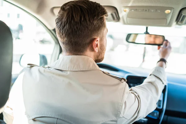 Driver looks in the rearview mirror. Man adjusts the mirror in the car