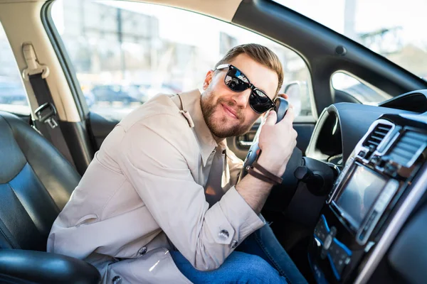 Satisfied man in sunglasses loves his car. Positive driver lies on the steering wheel of the auto