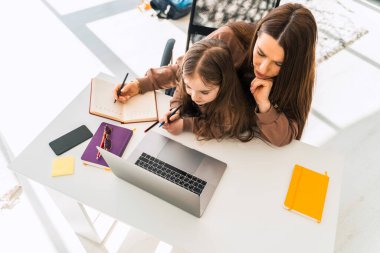 Anne ve kızı laptopun başında otururken ödev yapıyorlar.