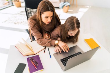 Anne ve küçük kızı laptopta ödev yapıyor. Anne çocuğuna evde öğretiyor.