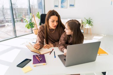 Anne ve küçük kızı laptopta ödev yapıyor. Anne çocuğuna evde öğretiyor.