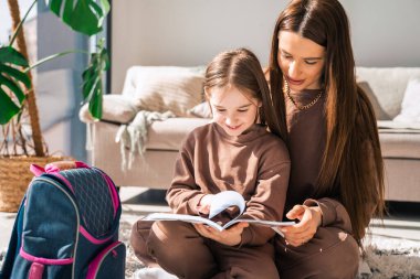 Anne ve kızı ödevlerini bir defterde okuyorlar.