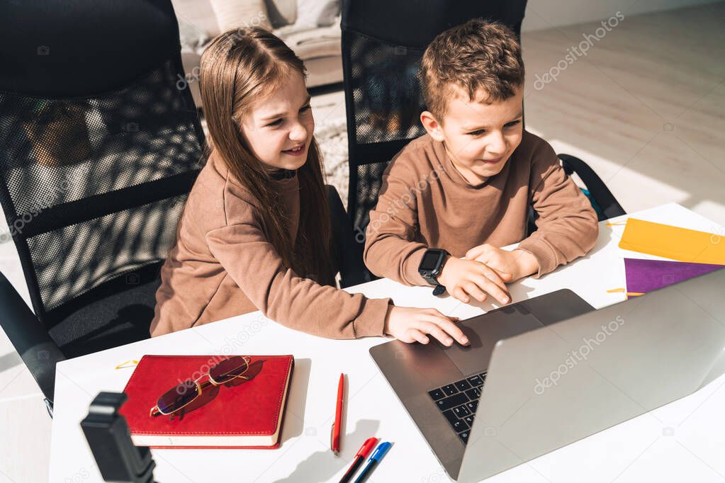 Little boy and girl study online in home at the laptop