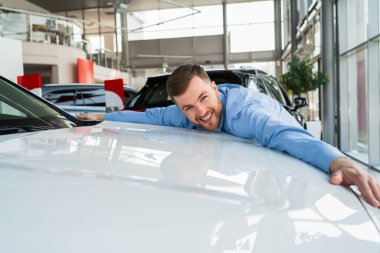 Yakışıklı adam bayilikte yeni arabaya sarılıyor.