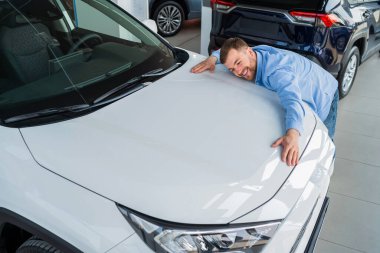 Yakışıklı adam bayilikte yeni arabaya sarılıyor.