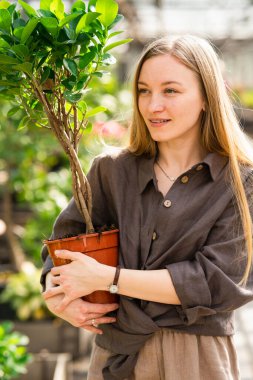 Bahçede çalışan, elinde saksı bitkisi olan güzel bir kadının portresi.