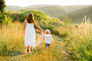 Anne ve oğlu tepedeki yeşil çimlerde yürüyorlar.