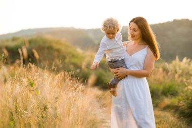 Kadın küçük oğluna güzel doğasını gösterir. Annem ve kollarında bir oğlan güzel manzaraların arka planına karşı
