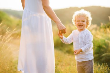 Doğada annesiyle yürürken sarı kıvırcık saçlı neşeli çocuk.